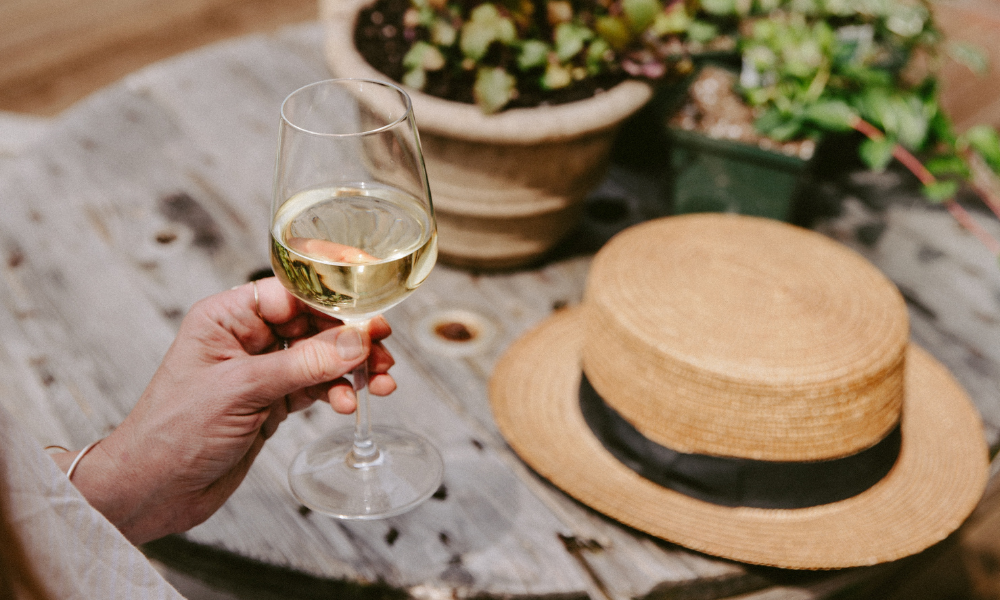 a glass of white Bordeaux in a man's hand with a hat in the background